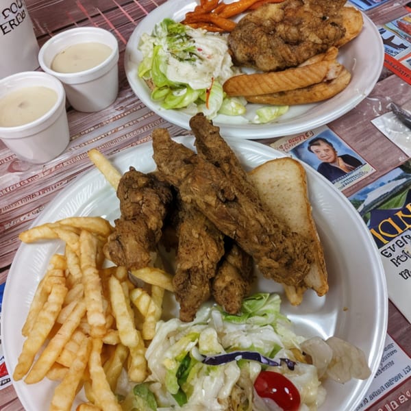 Two plates of Double J Eatery's fried chicken, fries, salad, and two cups of sauce.