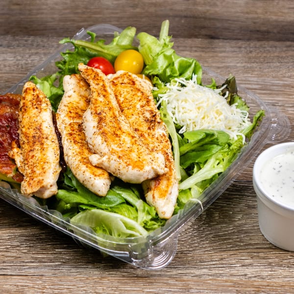 Grilled chicken salad with lettuce, tomatoes, shredded cheese, and dressing in a plastic container.
