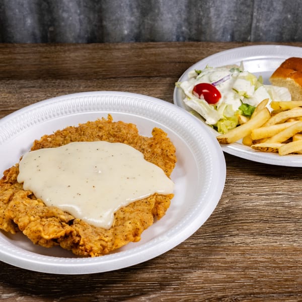 Chicken fried steak with gravy, fries, salad, and a roll on white plates at Double J Eatery.